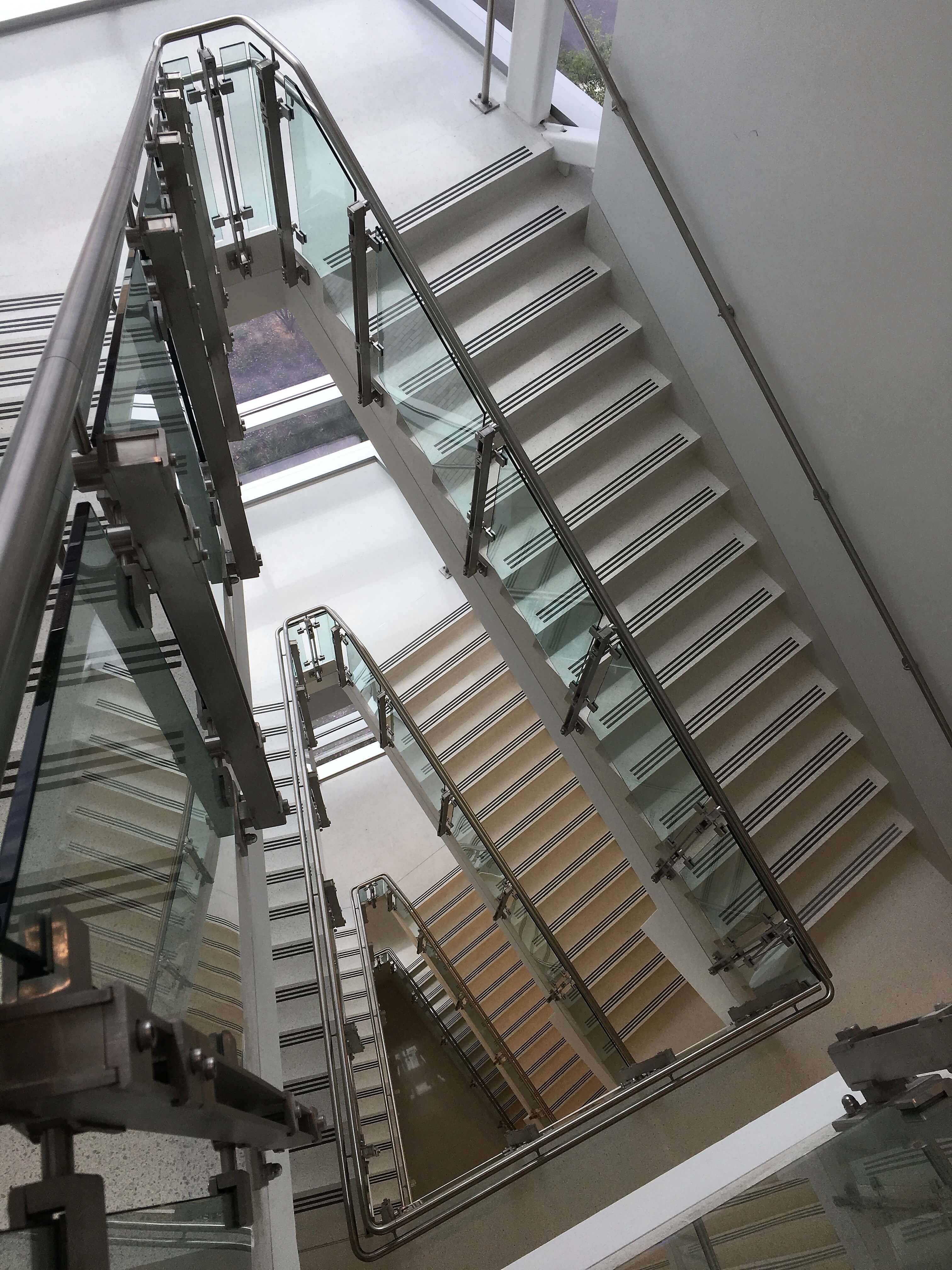 View down a stairwell of Inox guardrail with clear glass infill.