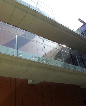 Outdoors side angled view at University of California San Diego, CA, Optik guardrail with clear glass and wood handrail