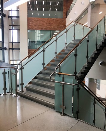 Circum guardrail installation with wood handrail and frosted glass infill at Texas State University, TX.