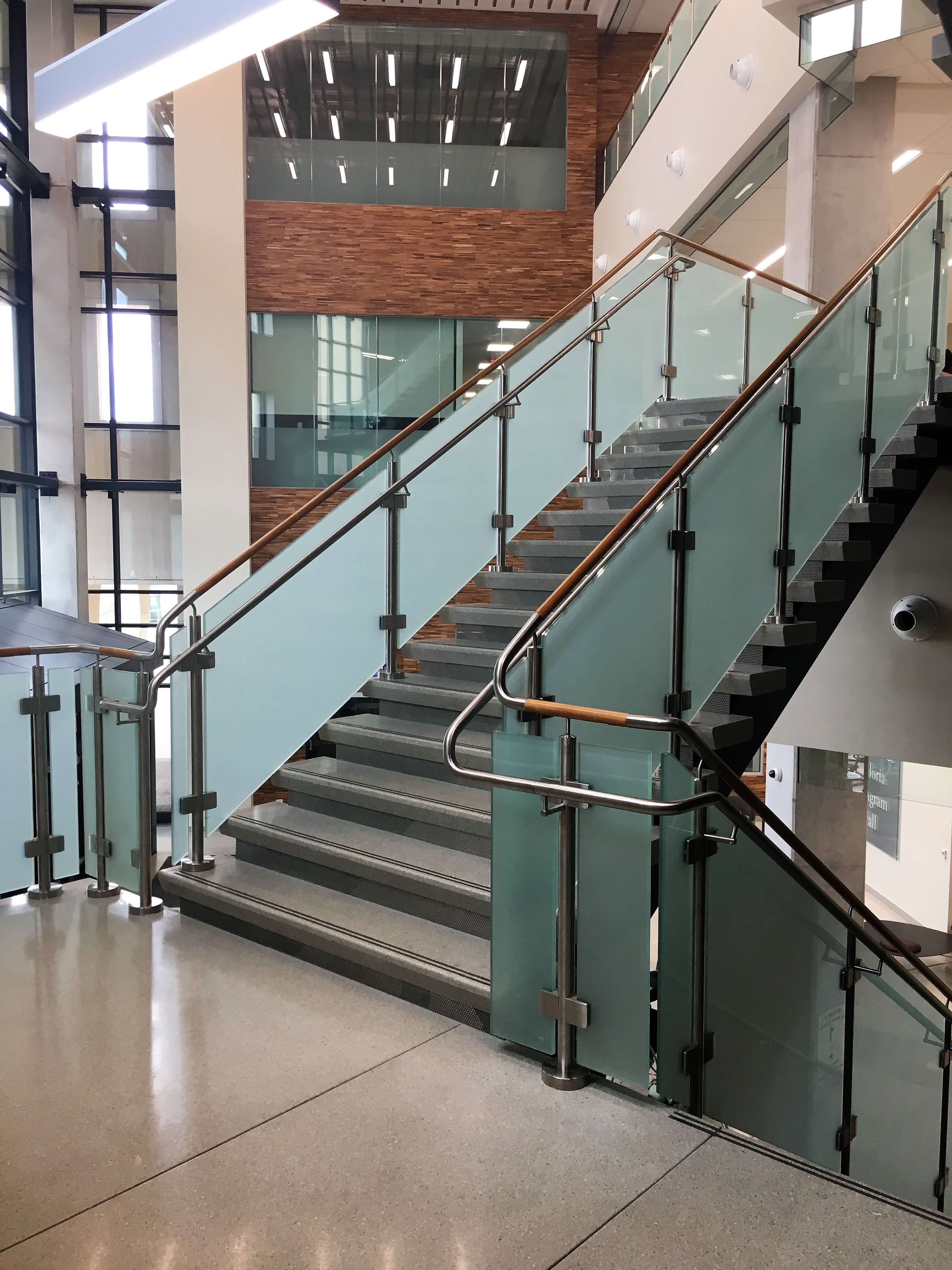 Circum guardrail installation with wood handrail and frosted glass infill at Texas State University, TX.